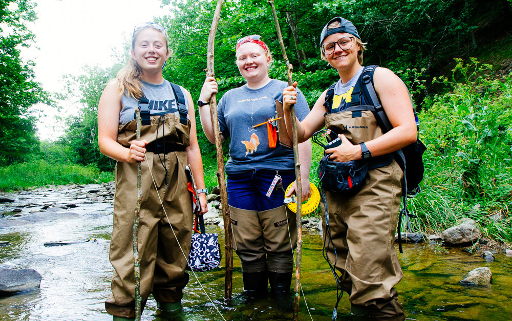 Three research students in river with poles and equipment 