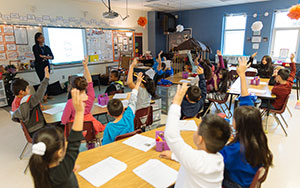 students with hands raised in a classroom